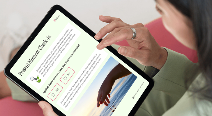 Person using a tablet to view a pastel-green “Present Moment Check-in” worksheet with highlighted Yes/No checkboxes and a hand touching water, seated on a pink sofa.